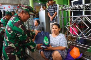 Personel TNI Kodim 0504 Jakarta Selatan menyerahkan bantuan tas biru berisi sembako kepada seorang warga wanita di Pejaten Timur saat banjir.