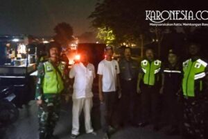 Anggota TNI Babinsa bersama personel Komponen Cadangan dan masyarakat melakukan koordinasi di pinggir jalan pada malam hari.