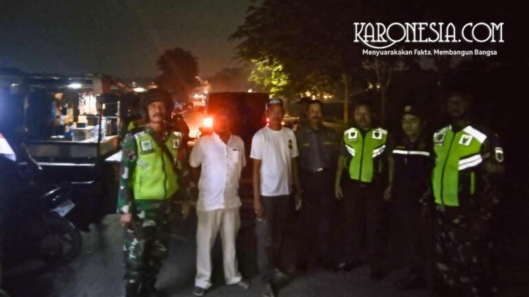 Anggota TNI Babinsa bersama personel Komponen Cadangan dan masyarakat melakukan koordinasi di pinggir jalan pada malam hari.