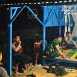 Personel Koramil 06 Cakung dan warga duduk bersama di pos siskamling saat patroli malam.