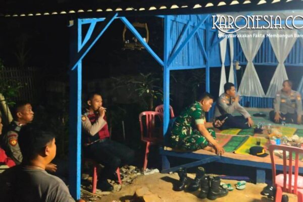 Personel Koramil 06 Cakung dan warga duduk bersama di pos siskamling saat patroli malam.