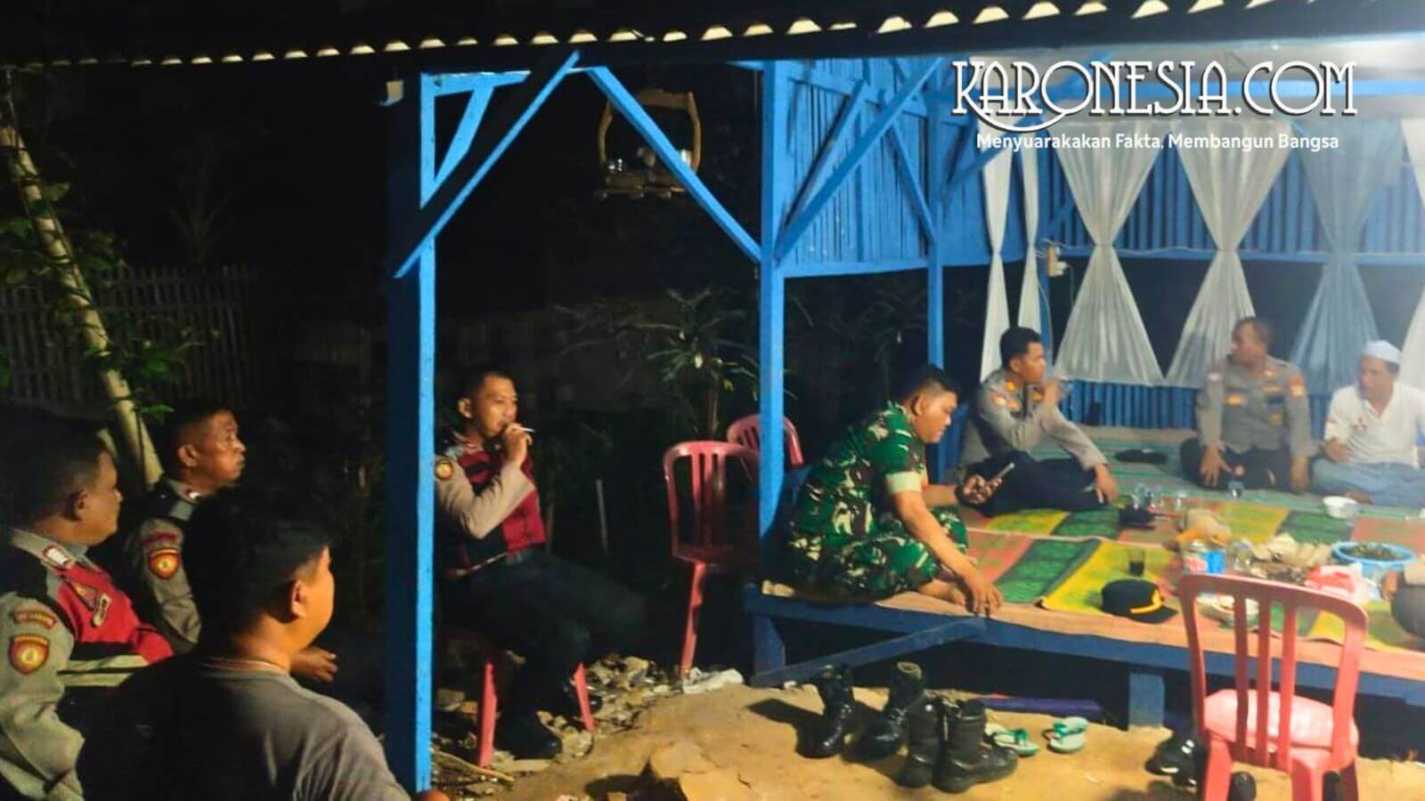 Personel Koramil 06 Cakung dan warga duduk bersama di pos siskamling saat patroli malam.