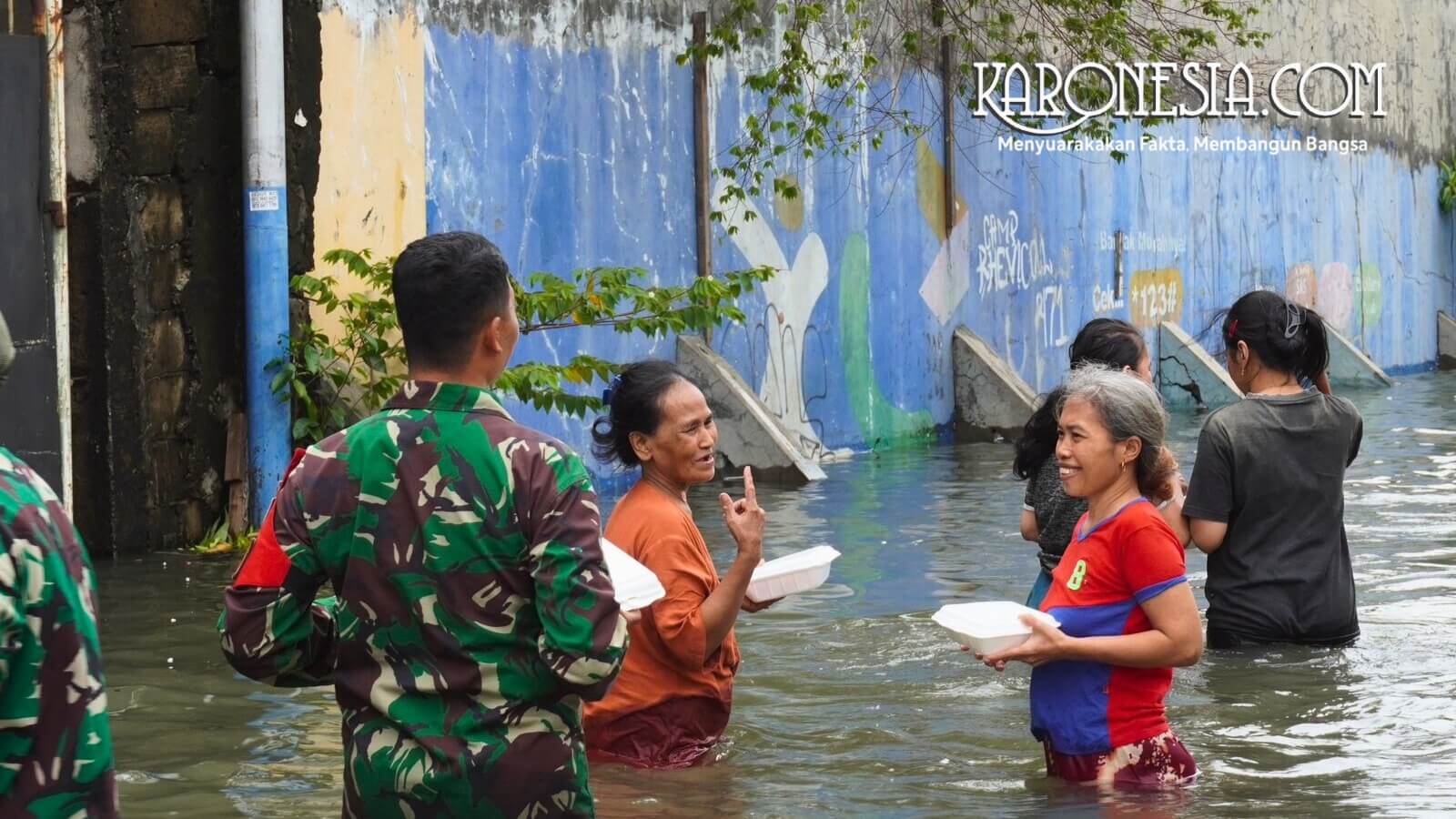 Prajurit TNI Kodam Jaya berinteraksi dengan warga saat distribusi bantuan makanan di lokasi banjir Kapuk Muara.