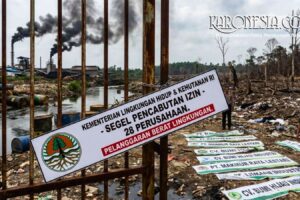 Penyegelan dari Kementerian Lingkungan Hidup & Kehutanan RI di depan pabrik yang mengeluarkan asap hitam pekat. Spanduk bertuliskan "SEGEL PENCABUTAN IZIN - 28 PERUSAHAAN - PELANGGARAN BERAT LINGKUNGAN"