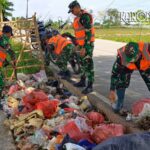Personel Koramil 08/Kronjo membersihkan sampah di pinggir jalan desa.
