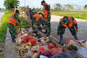 Personel Koramil 08/Kronjo membersihkan sampah di pinggir jalan desa.