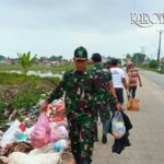 Personel TNI Koramil 08/Kronjo mengenakan seragam loreng sedang mengangkat kantong plastik berisi sampah di pinggir jalan Desa Muncung.