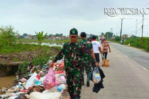 Personel TNI Koramil 08/Kronjo mengenakan seragam loreng sedang mengangkat kantong plastik berisi sampah di pinggir jalan Desa Muncung.