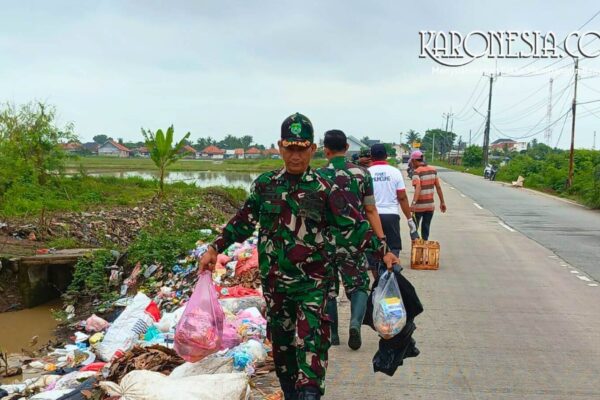 Personel TNI Koramil 08/Kronjo mengenakan seragam loreng sedang mengangkat kantong plastik berisi sampah di pinggir jalan Desa Muncung.