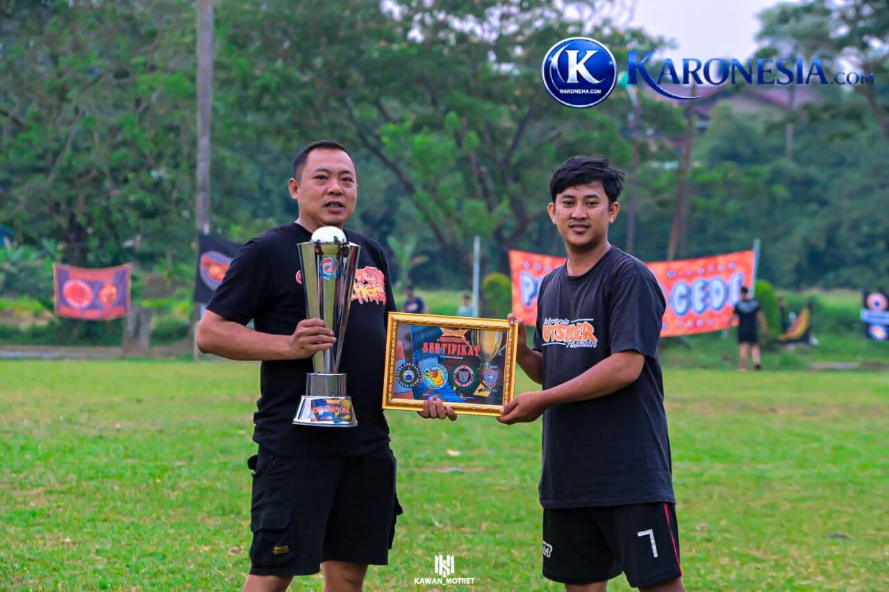Dua perwakilan suporter memegang piala dan piagam penghargaan di lapangan sepak bola.