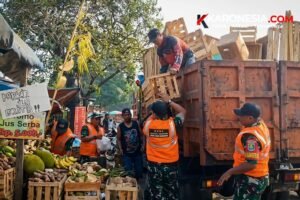 Personel Koramil 04/Ciledug berompi oranye bersama warga memindahkan kayu dan kardus bekas ke bak truk saat penanganan sampah di Pasar Lembang, Ciledug, Kota Tangerang.