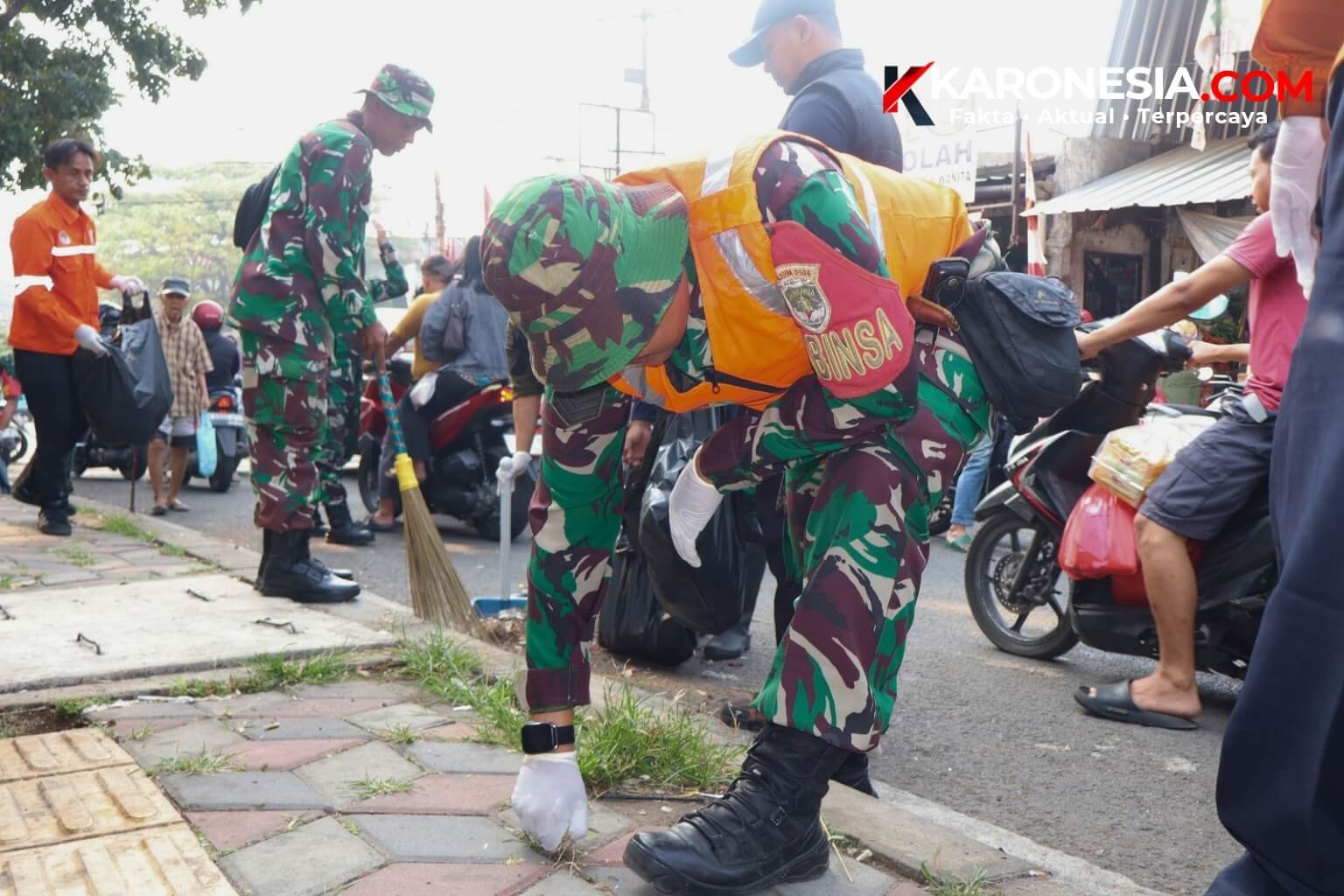 Personel Babinsa Koramil 05 Ciputat bersama tim gabungan memungut sampah di pinggir jalan kawasan Pasar Ciputat Tangsel.