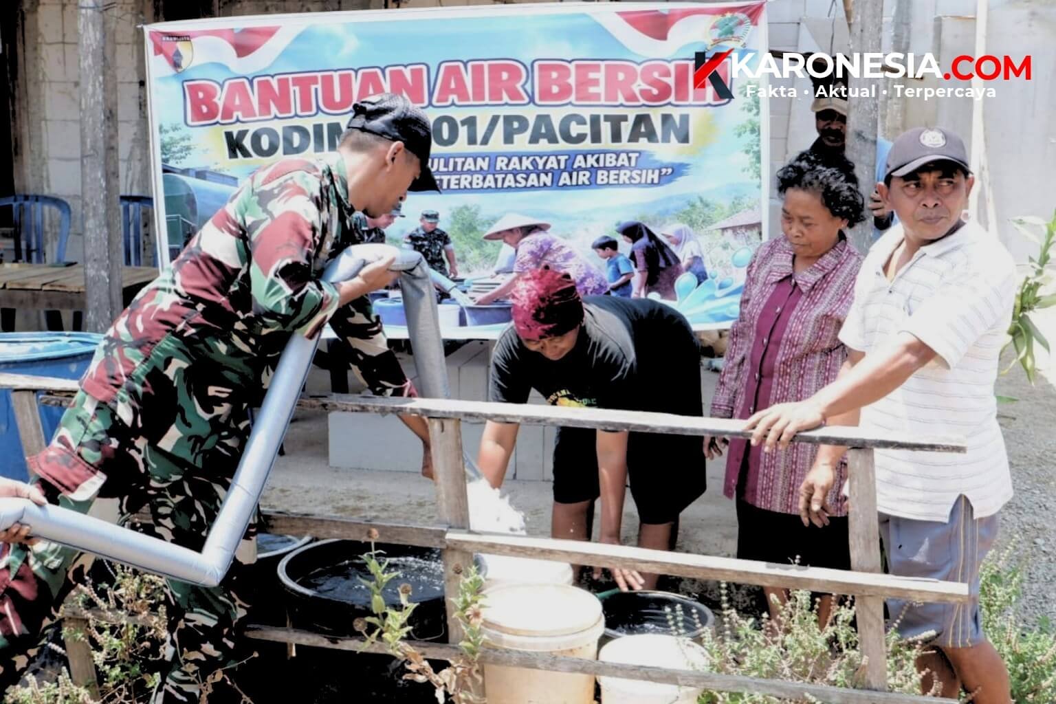 Prajurit TNI AD menyalurkan bantuan air bersih dengan selang ke wadah warga di depan spanduk Bantuan Air Bersih Kodim Pacitan, Korem 081/DSJ.