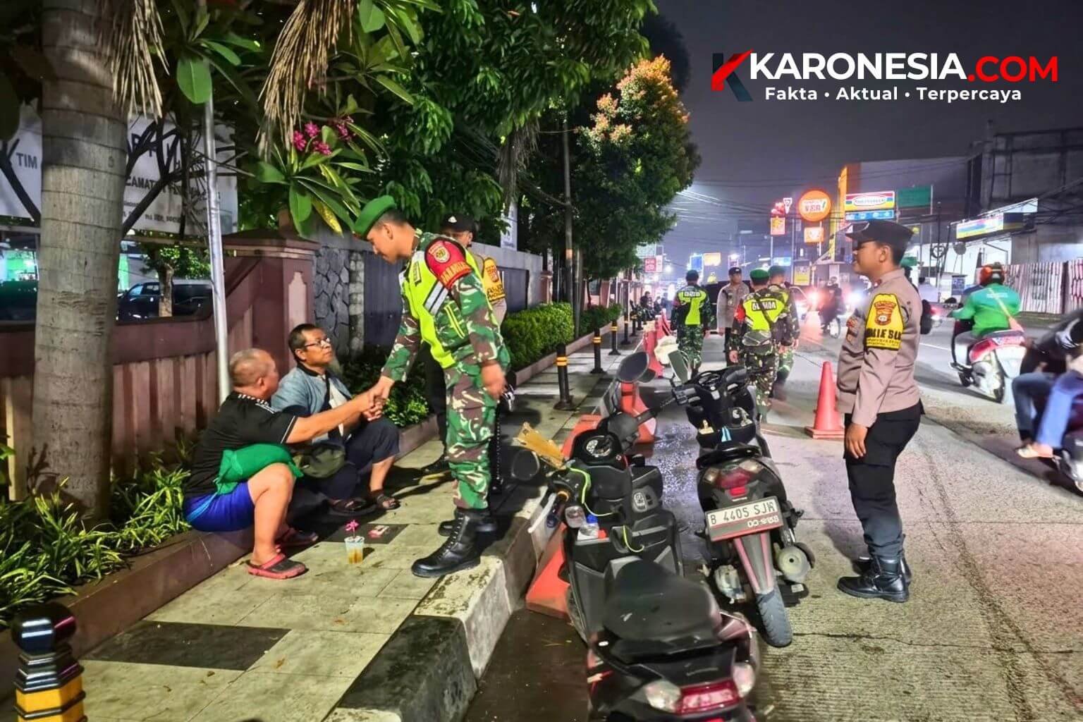 Anggota Babinsa TNI AD berseragam loreng menyalami dua warga yang duduk di trotoar saat patroli siskamling malam hari bersama personel berseragam lain.
