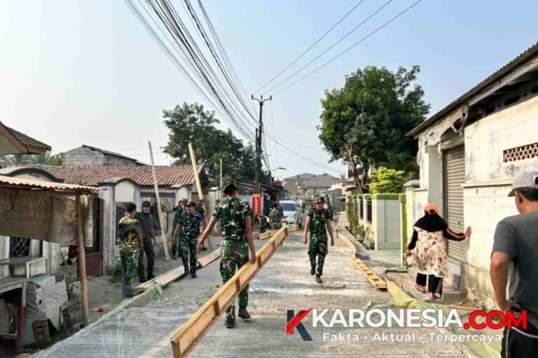 Personel TNI dan warga bekerja sama membawa cetakan bekisting jalan di depan area usaha warga Desa Sumur Bandung.