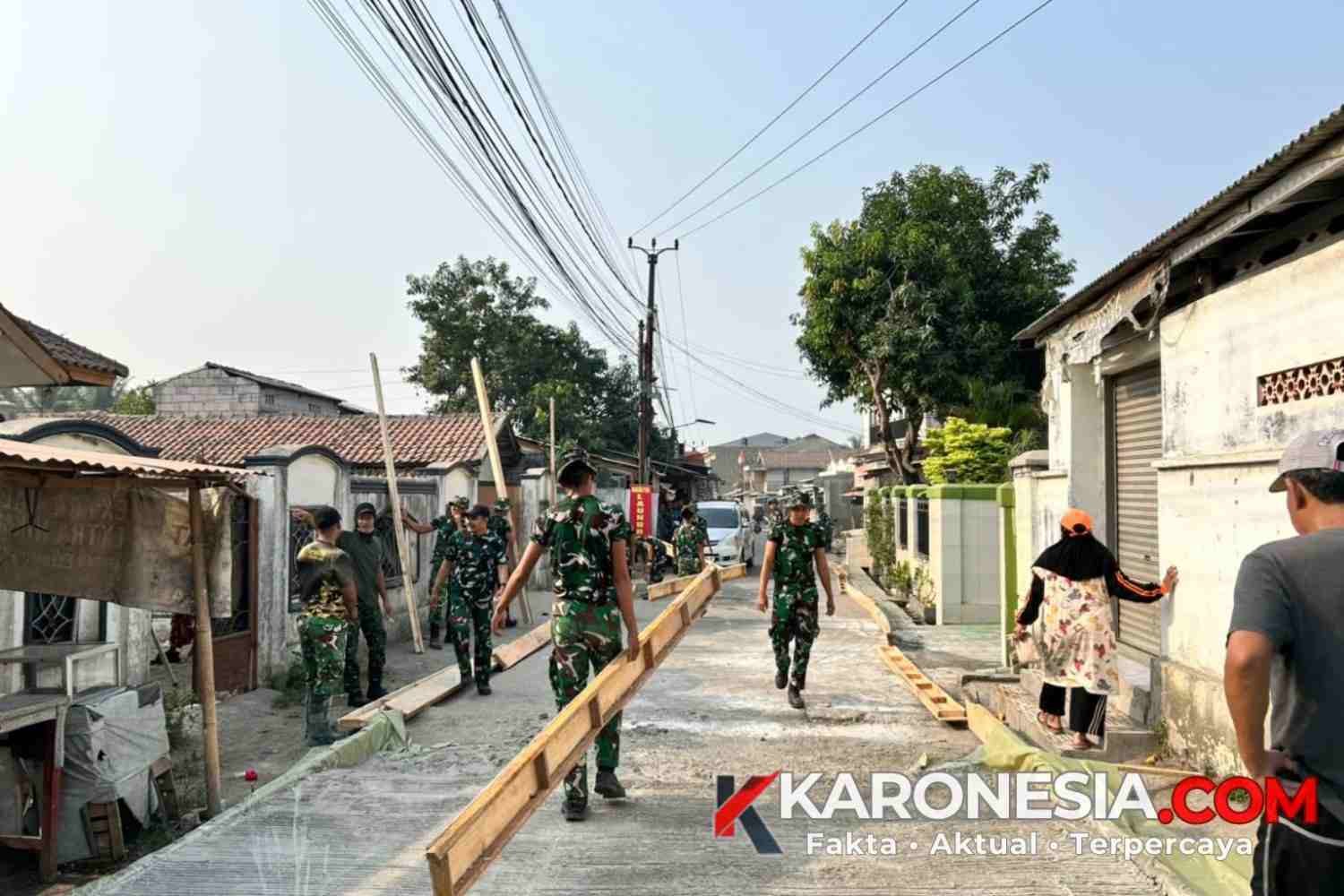Personel TNI dan warga bekerja sama membawa cetakan bekisting jalan di depan area usaha warga Desa Sumur Bandung.