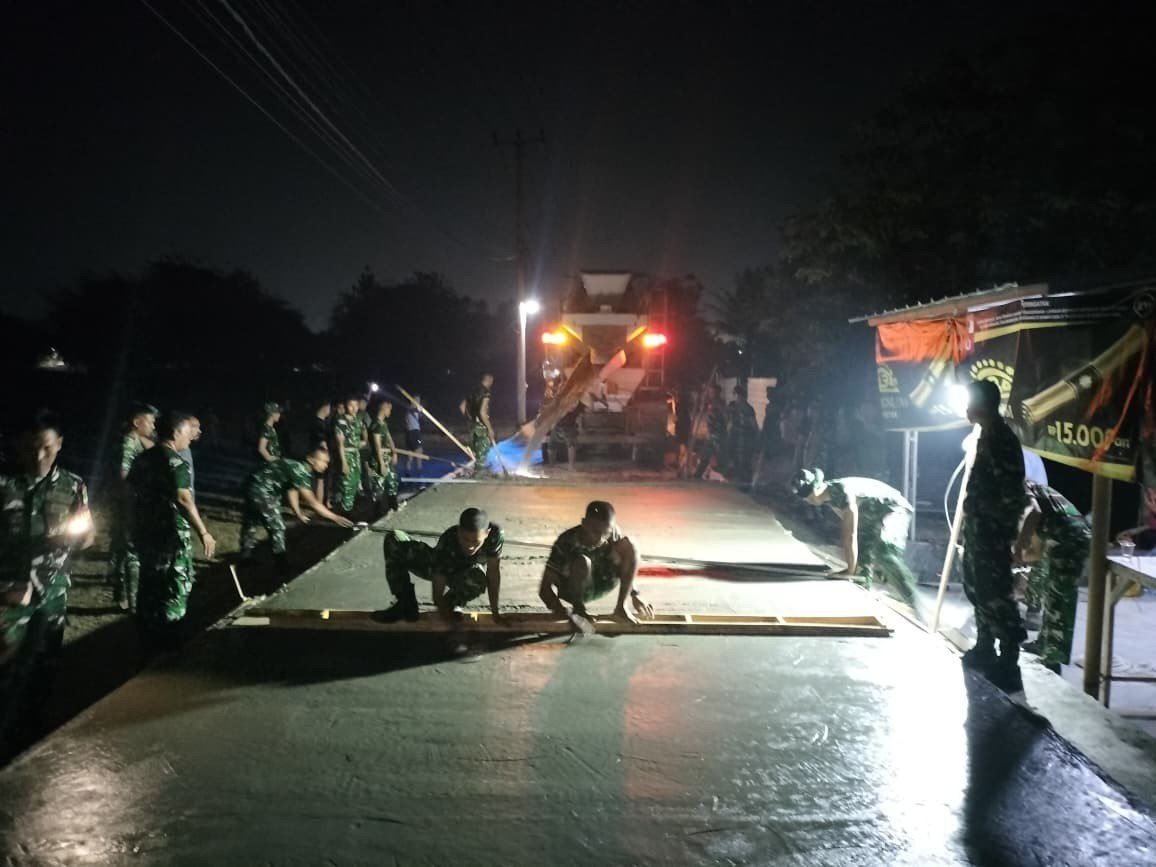 Puluhan prajurit TNI menggunakan seragam loreng bergotong royong melakukan pengecoran jalan desa menggunakan papan kayu pada malam hari dalam program TMMD Kodim Tigaraksa 2026.