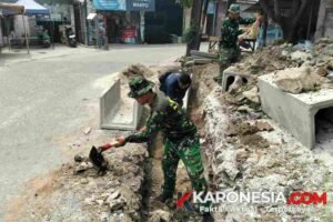 Anggota Satgas TMMD 130 Kodim 0510 Tigaraksa menggali tanah menggunakan cangkul untuk membuat parit drainase di Desa Sumur Bandung.