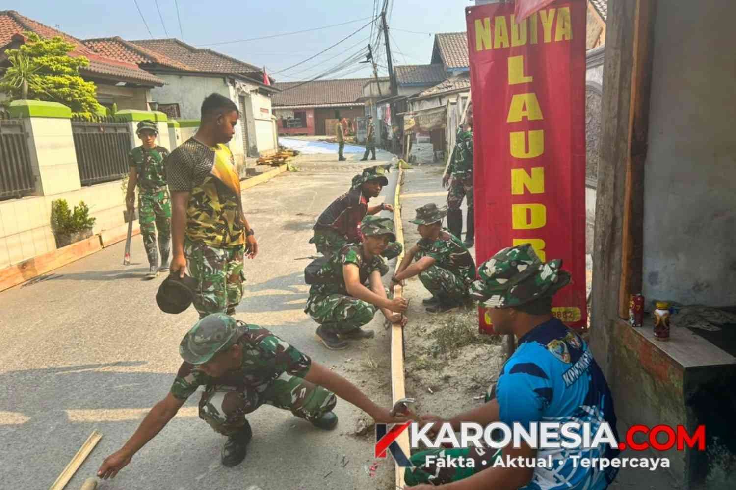 Prajurit Satgas TMMD Kodim 0510 Tigaraksa membahu papan bekisting kayu untuk persiapan pengecoran jalan desa.